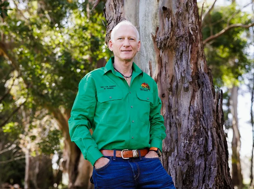 Robbie McKenzie in a green REALM work shirt, leaning on a gum tree on a farm